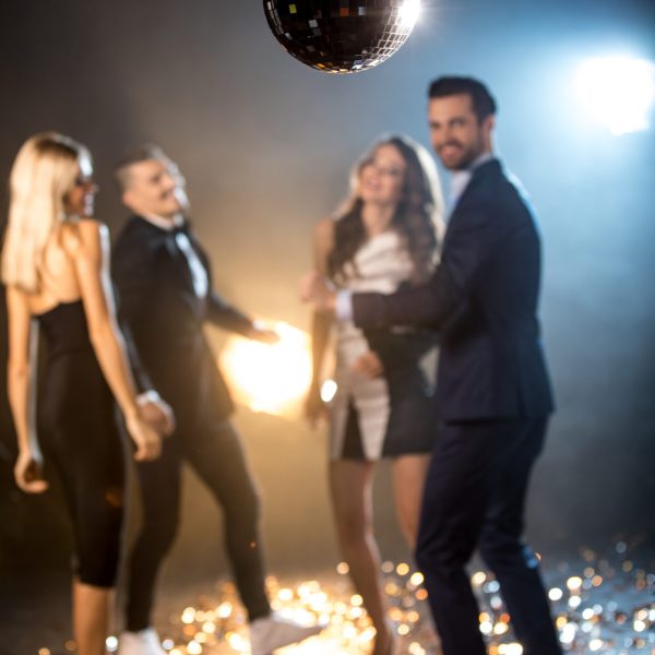 A lively group of people joyfully dancing around a shimmering disco ball at a vibrant party atmosphere.